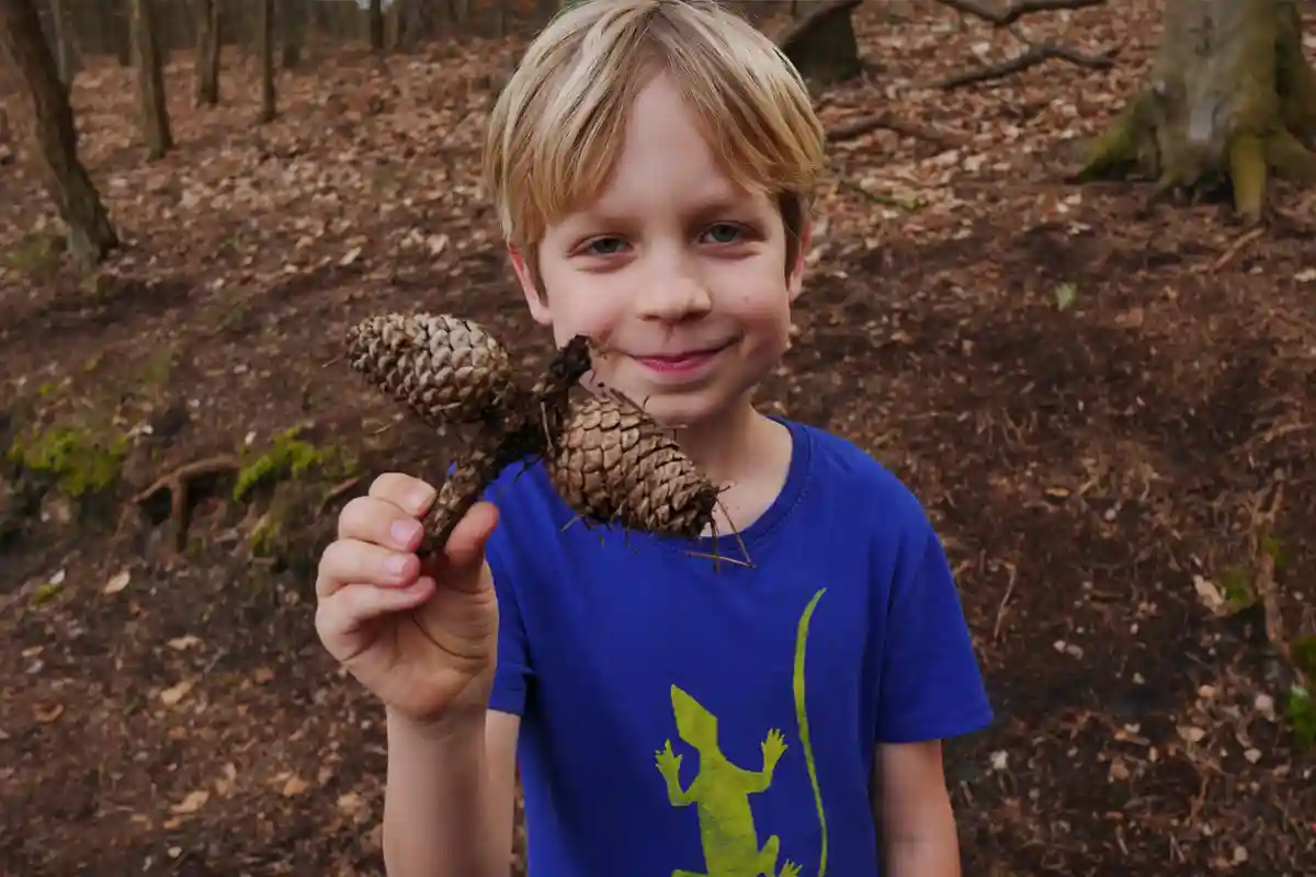 Ein Junge im Ostercamp von Wildnispfade hält stolz ein kreatives Gebilde aus Tannenzapfen im Wald.