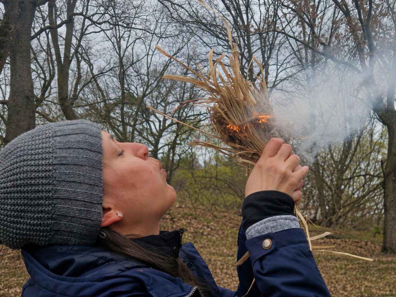 Eine Frau pustet ein Zundernest an zum Feuermachen.