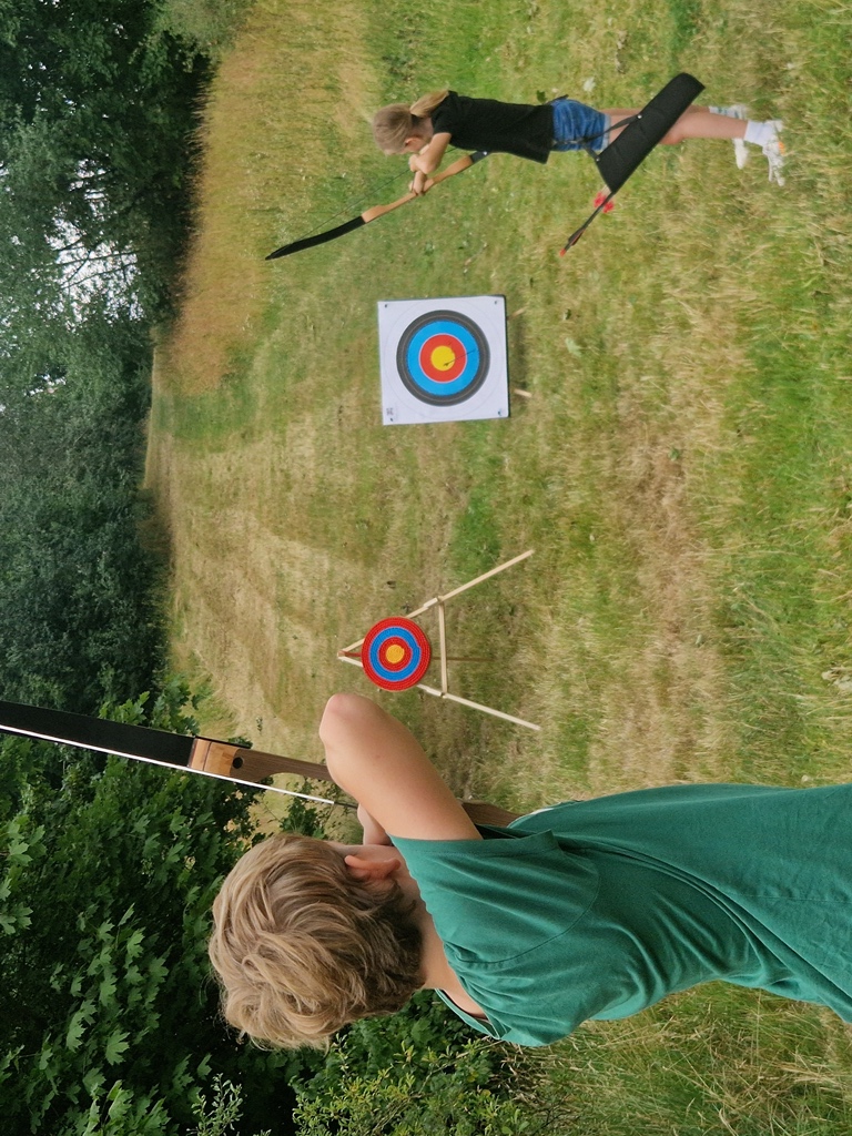 Kinder üben im Feriencamp das Bogenschießen.
