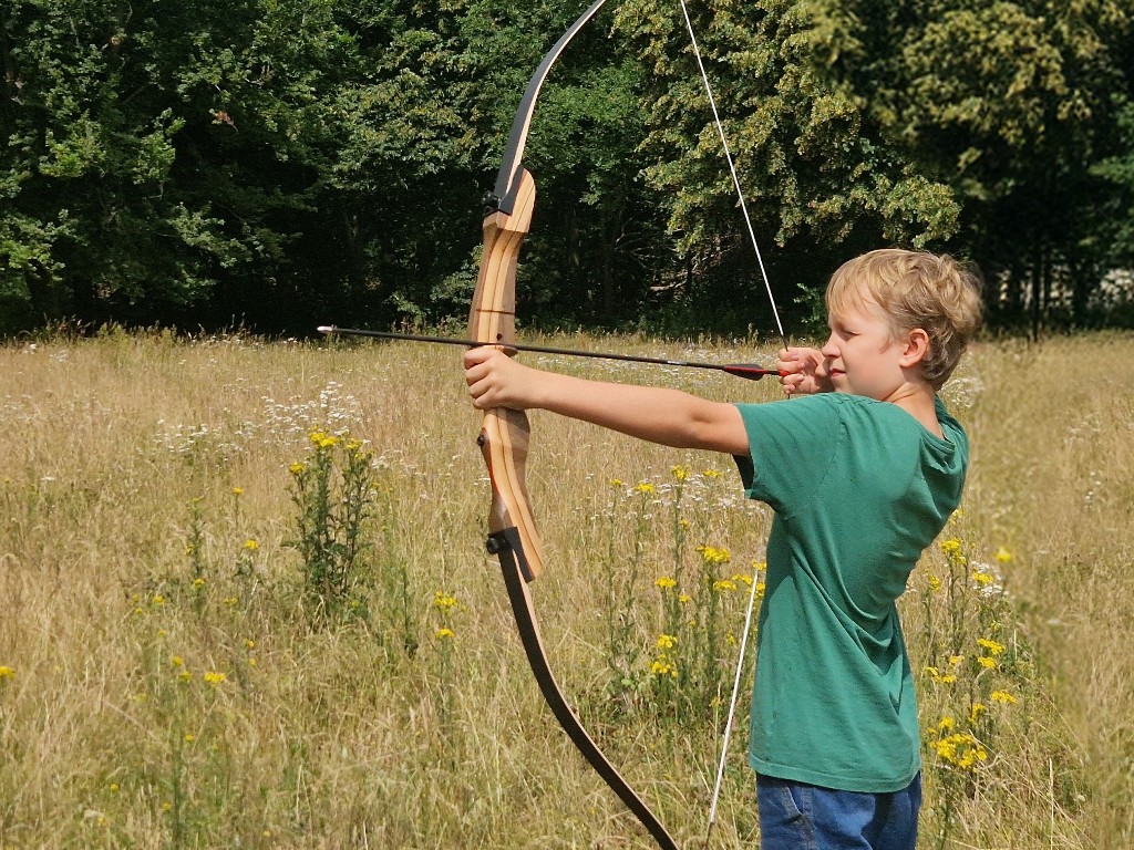 Ein Junge schießt einen Bogen auf einer Waldwiese.