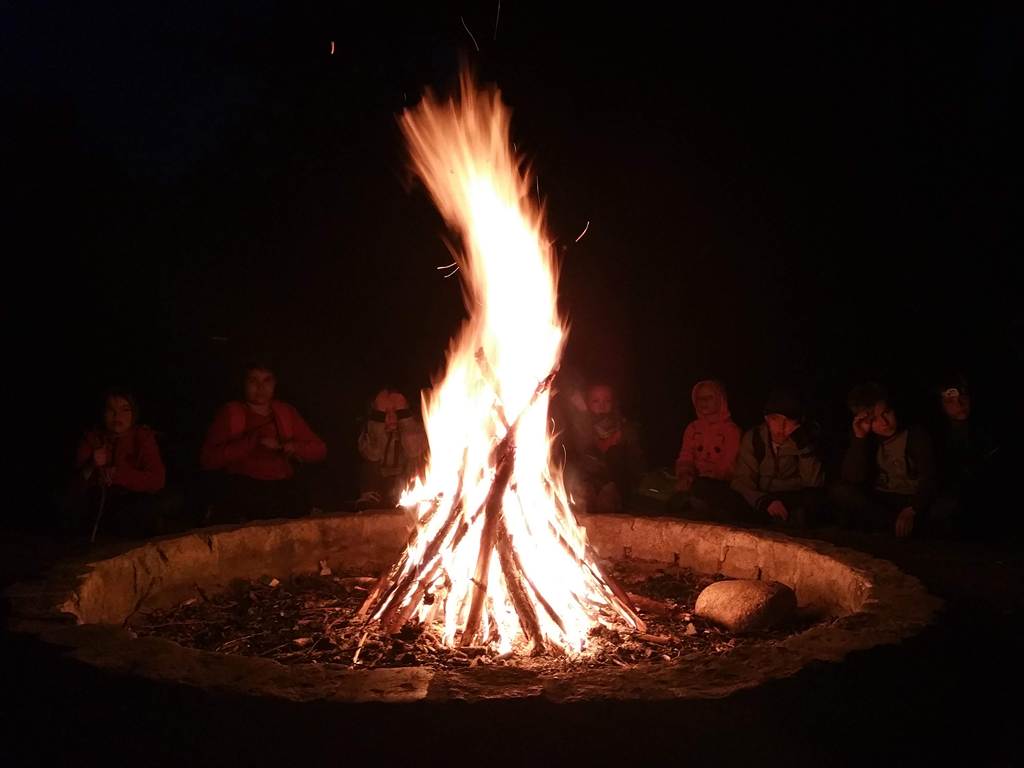 Eine Klasse sitzt abends im Dunkeln am Lagerfeuer.